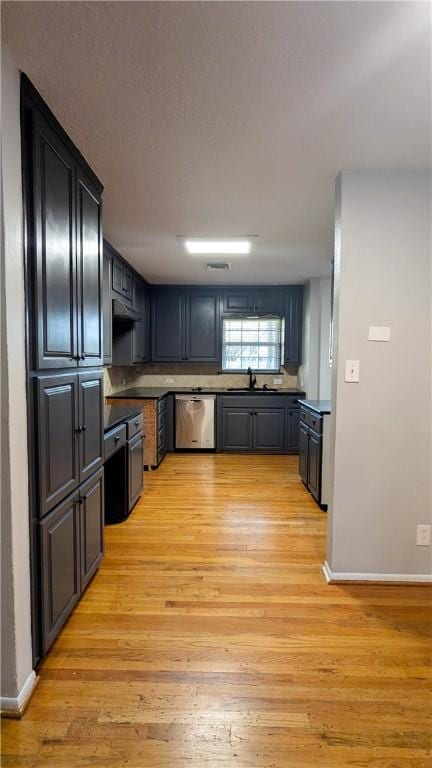 kitchen with light wood-style floors, a sink, dishwasher, under cabinet range hood, and baseboards