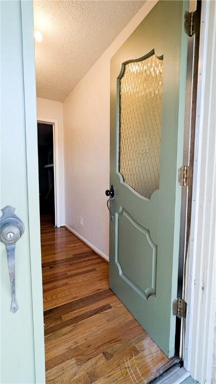 corridor with a textured ceiling and wood finished floors