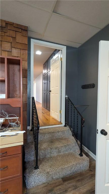 stairs with wood finished floors, a paneled ceiling, and baseboards