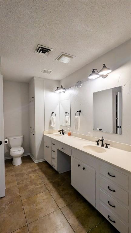 full bathroom featuring double vanity, visible vents, toilet, a sink, and a textured ceiling