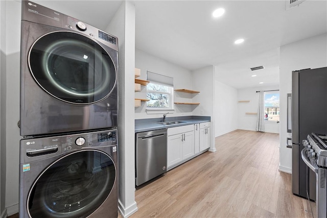 laundry area featuring stacked washer / dryer, light hardwood / wood-style flooring, a healthy amount of sunlight, and sink