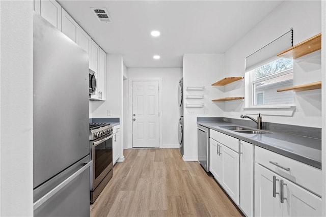 kitchen featuring stacked washer / drying machine, sink, white cabinetry, and stainless steel appliances