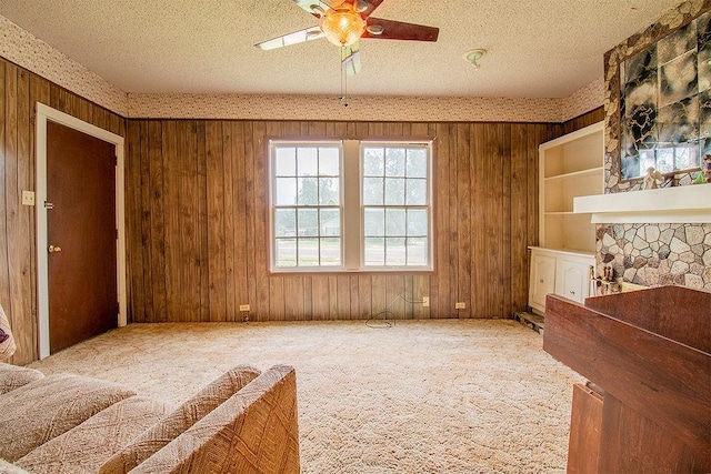 interior space featuring a textured ceiling, ceiling fan, a fireplace, carpet floors, and wood walls