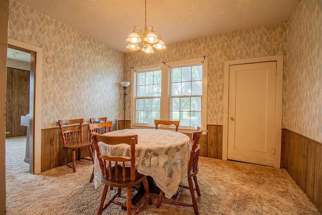 carpeted dining space with a textured ceiling, an inviting chandelier, and wood walls