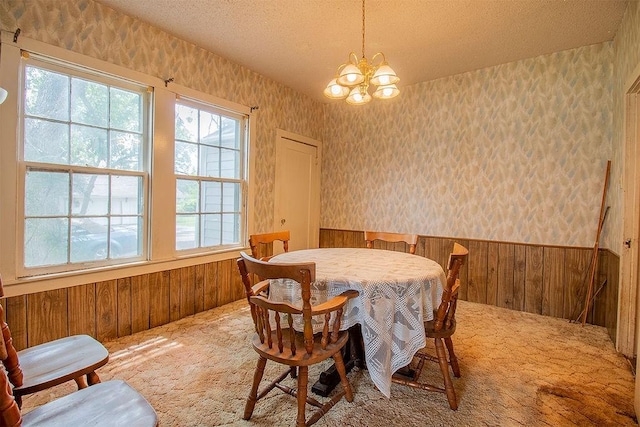 dining room featuring wooden walls, carpet, a chandelier, and a textured ceiling