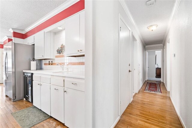 kitchen featuring white cabinets, light wood-type flooring, crown molding, and sink