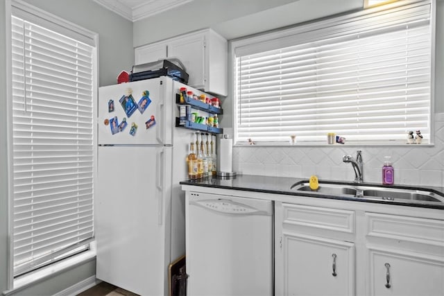 kitchen with white appliances, dark countertops, a sink, white cabinetry, and crown molding