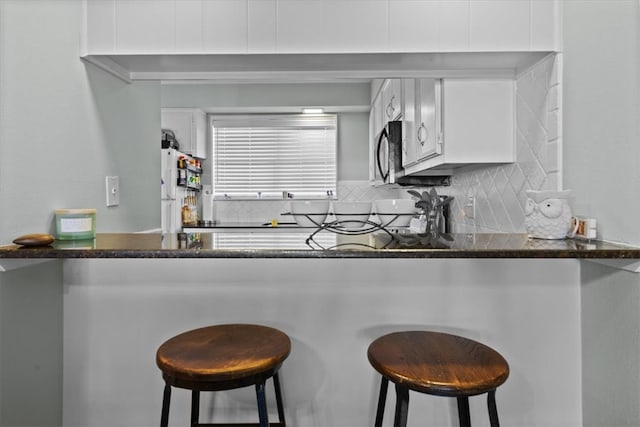 kitchen featuring white cabinetry, dark countertops, tasteful backsplash, and freestanding refrigerator