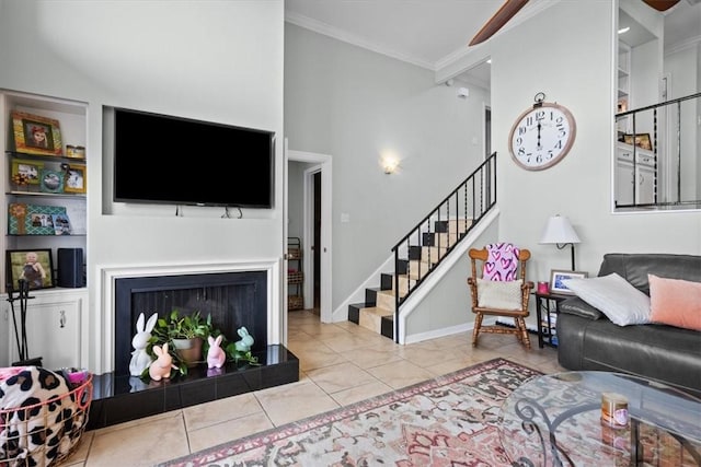 tiled living room with built in shelves, baseboards, a fireplace with raised hearth, ornamental molding, and stairs