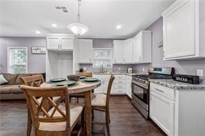 kitchen featuring dark wood-type flooring, hanging light fixtures, gas range, light stone counters, and white cabinetry