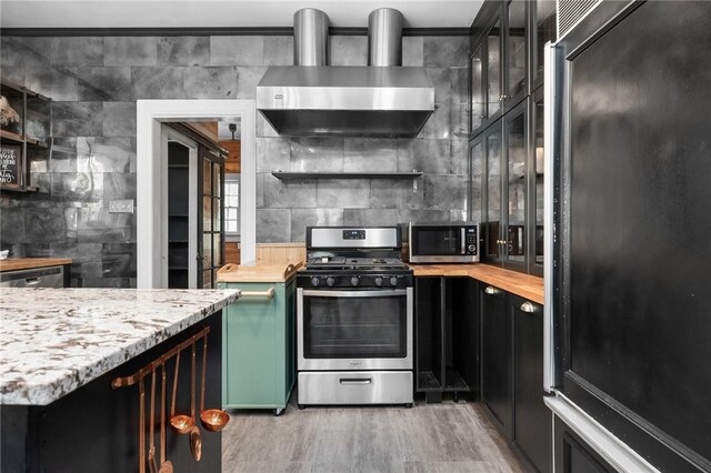 kitchen with wall chimney exhaust hood, light stone countertops, wood-type flooring, and appliances with stainless steel finishes