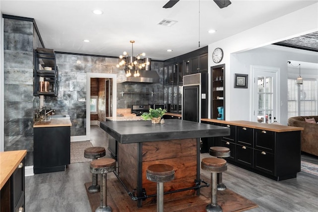 kitchen with stainless steel range with electric stovetop, a kitchen bar, wall chimney exhaust hood, paneled fridge, and dark hardwood / wood-style flooring