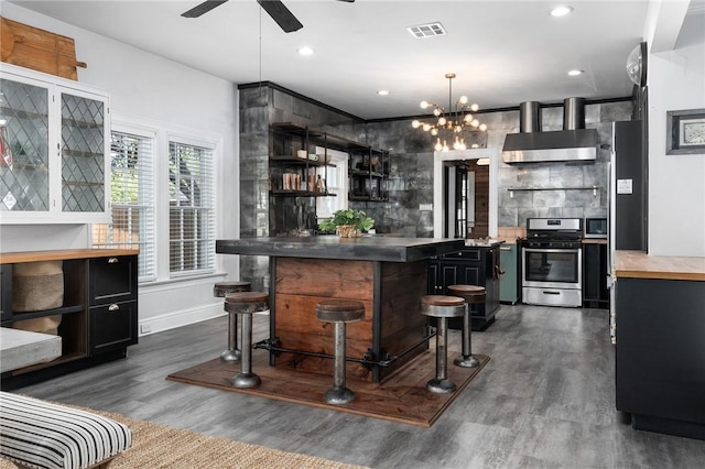 bar featuring ceiling fan with notable chandelier, stainless steel appliances, dark wood-type flooring, and wall chimney range hood