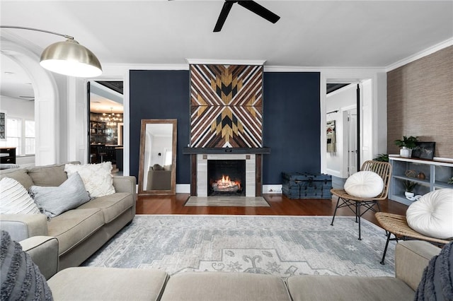 living room with a fireplace, wood-type flooring, ceiling fan, and crown molding