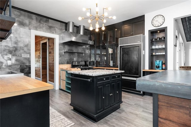 kitchen featuring light wood-type flooring, stainless steel appliances, wall chimney range hood, a center island, and hanging light fixtures