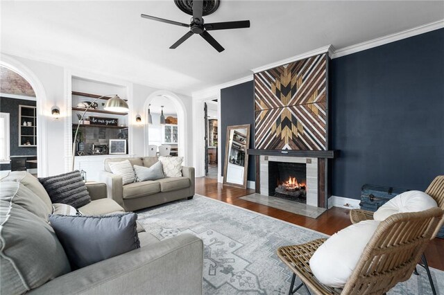 living room with ceiling fan, a large fireplace, dark hardwood / wood-style floors, and ornamental molding