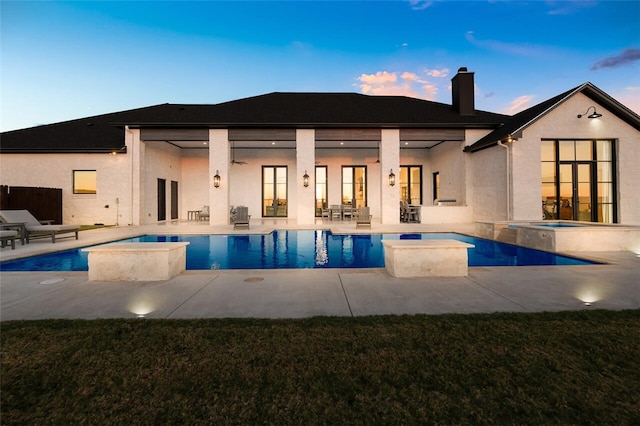 back house at dusk with a swimming pool with hot tub and a patio