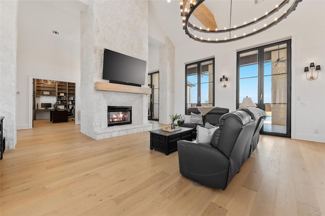 living room with french doors, light hardwood / wood-style flooring, a notable chandelier, a towering ceiling, and a fireplace