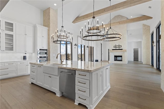 kitchen with appliances with stainless steel finishes, light wood-type flooring, light stone counters, white cabinets, and hanging light fixtures