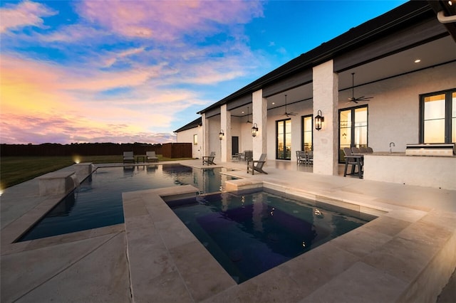 pool at dusk featuring area for grilling, ceiling fan, a bar, a patio, and a hot tub