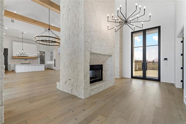 living room with beamed ceiling, a high ceiling, light hardwood / wood-style floors, and a premium fireplace