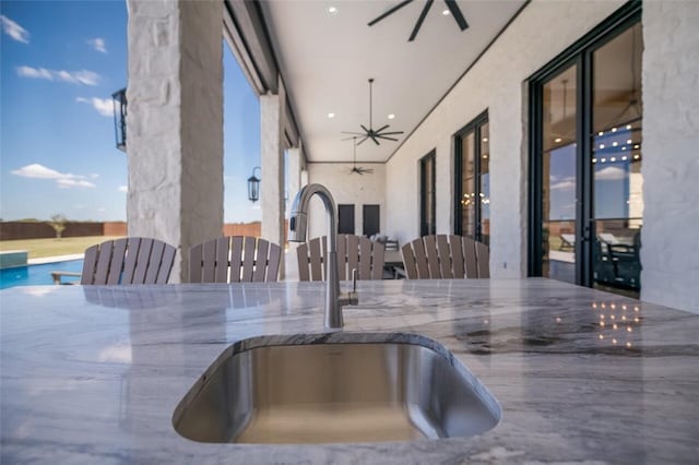 kitchen featuring ceiling fan, sink, and stone countertops