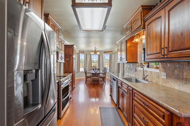 kitchen with tasteful backsplash, stainless steel appliances, sink, wood-type flooring, and pendant lighting