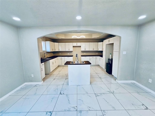 kitchen with arched walkways, a sink, marble finish floor, stainless steel dishwasher, and dark countertops