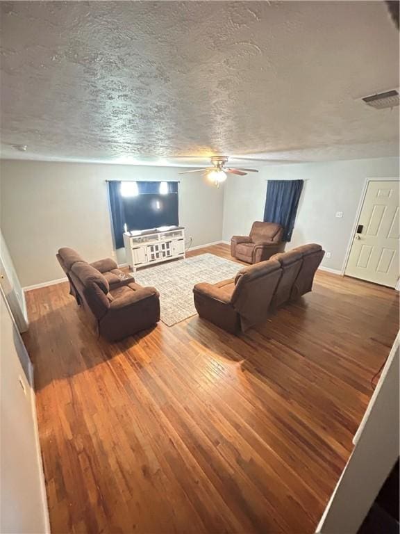 living area featuring wood finished floors, visible vents, baseboards, ceiling fan, and a textured ceiling