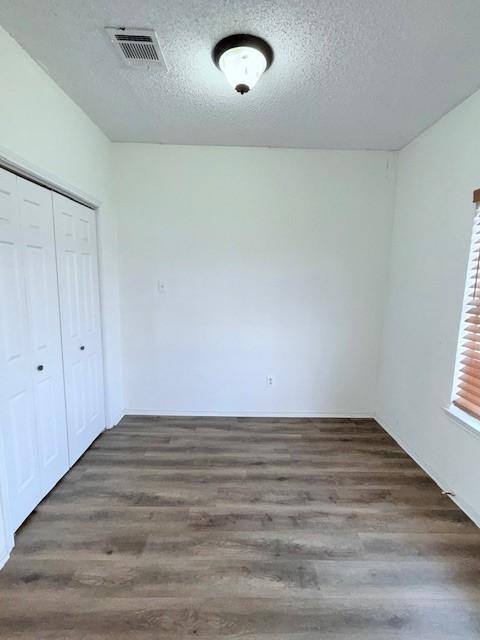 unfurnished bedroom featuring dark hardwood / wood-style flooring, a textured ceiling, and a closet