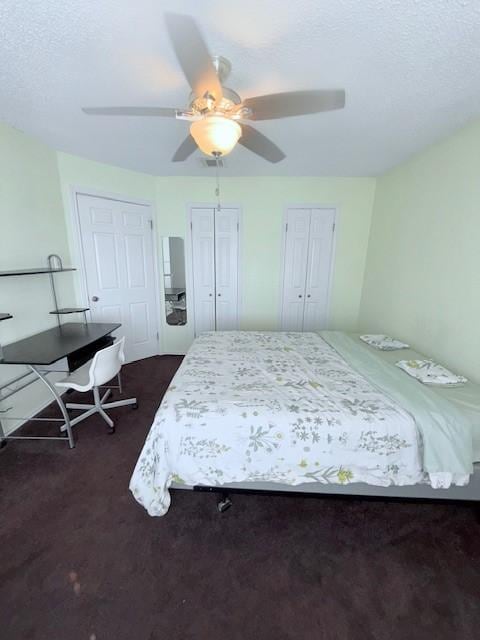 bedroom with two closets, a textured ceiling, ceiling fan, and dark colored carpet