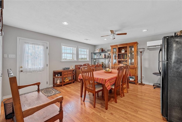 dining space with a wall mounted AC, light wood-type flooring, and ceiling fan