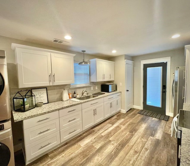 kitchen with sink, stacked washer / dryer, and white cabinets