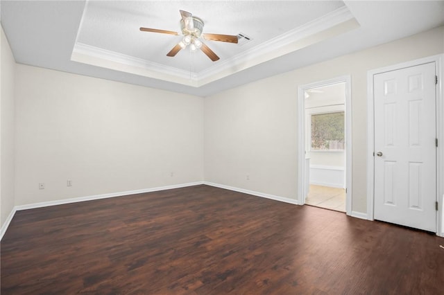 empty room featuring a tray ceiling, crown molding, ceiling fan, and dark wood-type flooring