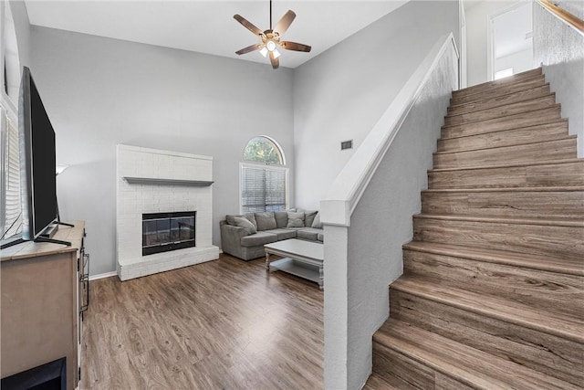 stairs featuring ceiling fan, a fireplace, a towering ceiling, and hardwood / wood-style flooring