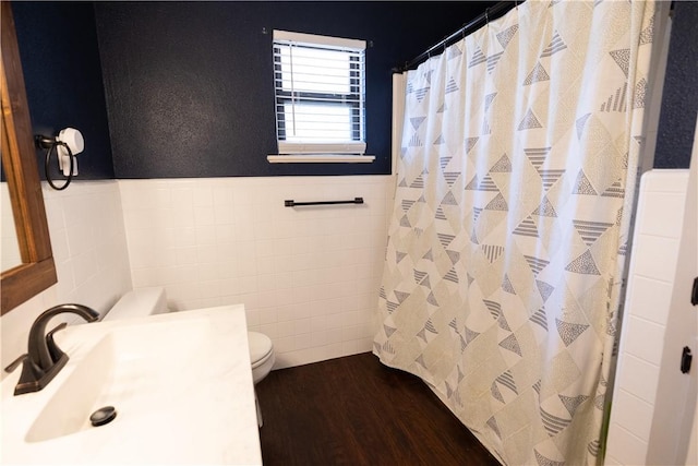 bathroom featuring wood finished floors, a sink, wainscoting, tile walls, and toilet