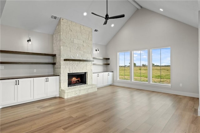 unfurnished living room with ceiling fan, high vaulted ceiling, beamed ceiling, light hardwood / wood-style floors, and a stone fireplace