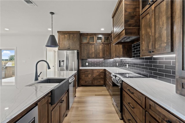 kitchen with sink, hanging light fixtures, light wood-type flooring, light stone countertops, and stainless steel appliances