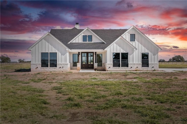 back house at dusk featuring french doors and a yard