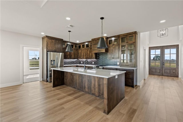 kitchen with premium range hood, light wood-type flooring, an island with sink, and appliances with stainless steel finishes