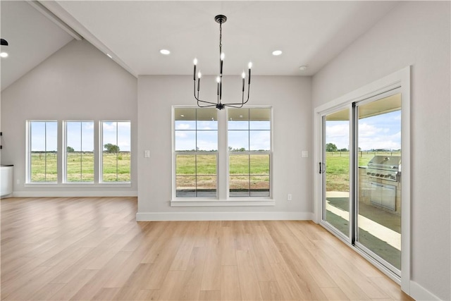 unfurnished dining area with light wood-type flooring, high vaulted ceiling, and a chandelier