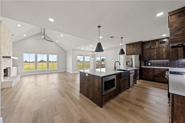 kitchen with a center island with sink, light wood-type flooring, a fireplace, appliances with stainless steel finishes, and tasteful backsplash