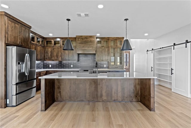 kitchen with stainless steel refrigerator with ice dispenser, a barn door, a center island with sink, and light hardwood / wood-style floors