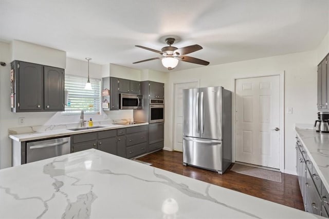 kitchen with appliances with stainless steel finishes, dark hardwood / wood-style flooring, light stone counters, sink, and decorative light fixtures