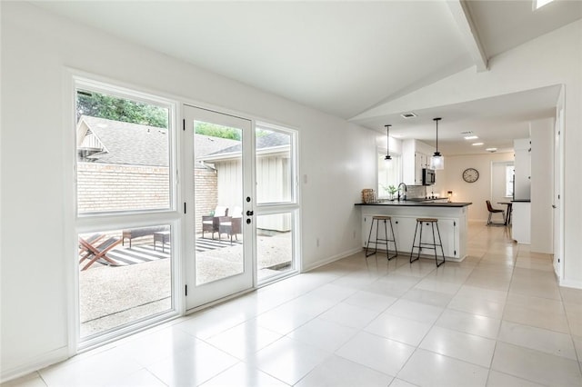 interior space with pendant lighting, white cabinets, lofted ceiling with beams, kitchen peninsula, and a breakfast bar area