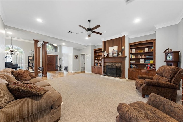 carpeted living room featuring ornate columns, crown molding, a fireplace, and ceiling fan with notable chandelier