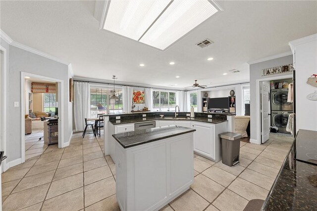 kitchen featuring kitchen peninsula, ceiling fan, crown molding, pendant lighting, and stacked washer / dryer