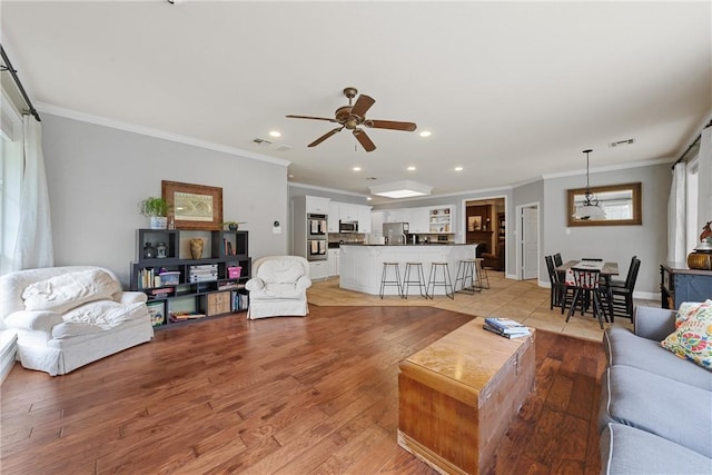 living room featuring a wealth of natural light, ceiling fan, ornamental molding, and light wood-type flooring