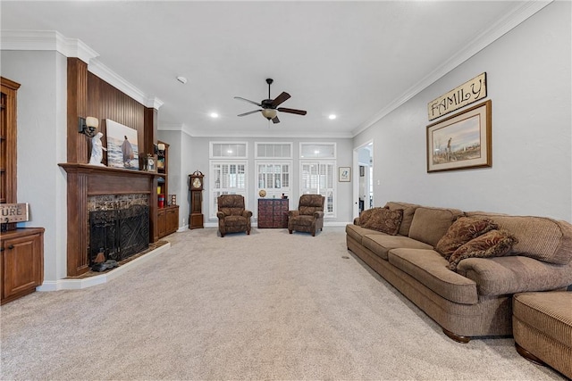 carpeted living room with ceiling fan, a stone fireplace, and crown molding