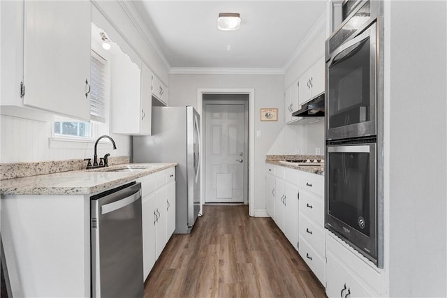 kitchen with a sink, under cabinet range hood, appliances with stainless steel finishes, white cabinetry, and crown molding